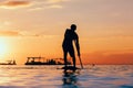 Black sunset silhouette of paddle boarder standing on SUP