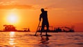 Black sunset silhouette of paddle boarder standing on SUP