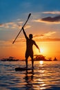 Black sunset silhouette of paddle boarder standing on SUP