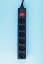 A black surge protector with portable sockets and a red button on a blue background.