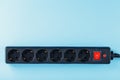 A black surge protector with portable sockets and a red button on a blue background.