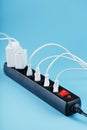 Black surge protector with a red button and connected white wires of electrical appliances on a blue background. Royalty Free Stock Photo
