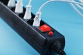 Black surge protector with a red button and connected white wires of electrical appliances on a blue background. Royalty Free Stock Photo