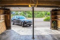 Black Suv turning into garage with automatic overhead door opener - grainy unfinished surfaces and pavement - Suburban