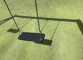 Black swing on green grass at the playground. Green coating on the sports ground. Place to add text Royalty Free Stock Photo