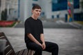 Black t-shirt mockup on a young guy sitting on a bench on a blurred background in the park, stylish clothes for design Royalty Free Stock Photo