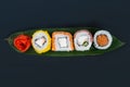 On a black table, on a bamboo leaf, assorted Japanese rolls of tuna, salmon, soft cheese, baked in tempura and pickled ginger in Royalty Free Stock Photo