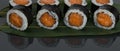 On a black table with a reflection, on a bamboo leaf, Japanese salmon rolls are laid out in a row