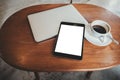 A black tablet pc with blank desktop white screen with laptop and coffee cup on wooden table Royalty Free Stock Photo