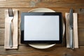 Black tablet PC on dinner table with plate, fork, and knife Royalty Free Stock Photo