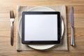 Black tablet PC on dinner table with plate, fork, and knife Royalty Free Stock Photo