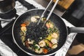 Black tagliolini pasta added to fried shrimps and cherry tomatoes. Restaurant dish. Chef using cooking tongs. Royalty Free Stock Photo