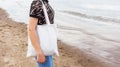 black tanned girl holding tote eco bag close up canvas fabric for mockup. young woman stands against of sand coast