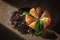 Black tea with bergamot is scattered in the shape of a circle. Mandarin and three green leaves adorn the composition.