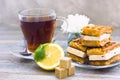 Black tea ceremony - waffles, glass full of tea, glass pot, sugar, yellow lemon, flower, tea leaves, spices on a wooden boards