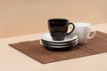 Black tea cup on the stack of the white and black plates near white tea cup on tablemat. Royalty Free Stock Photo