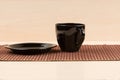 Black tea cup standing near black plate on tablemat.