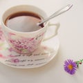 Black tea with spoon in an elegant vintage porcelain cup on the white table. Delicate violet flower chrysanthemum near