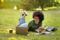 Black teenage girl lying on grass at park, studying, using laptop computer Royalty Free Stock Photo