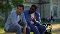 Black teenager male ignoring scolding dad sitting on campus bench, conflict