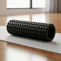 A black textured foam roller rests on a light-colored yoga mat, positioned on a wooden floor. The Royalty Free Stock Photo