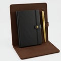 Black Textured Notebook and Golden Pen Leaning Against Brown Folder Isolated on White Royalty Free Stock Photo