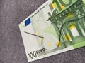 Black thread with a needle are on the 100 euro banknote. The background is fabric grey. The banknote lies at an angle