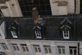 Black tiled high roof with white thin windows sticking out the roof and one brick chimney in the middle