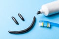Black toothpaste from charcoal for white teeth. Toothpaste in the form of smile on the face, tube and toothbrush on blue Royalty Free Stock Photo