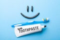 Black toothpaste from charcoal for white teeth. Toothpaste in the form of smile on the face, tube and toothbrush on blue Royalty Free Stock Photo