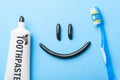 Black toothpaste from charcoal for white teeth. Toothpaste in the form of smile on the face, tube and toothbrush on blue