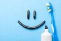 Black toothpaste from charcoal for white teeth. Toothpaste in the form of smile on the face, tube and toothbrush on blue Royalty Free Stock Photo