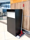 Black trash bin and cleaning mop placed beside a wooden panel in a bright modern cafeteria interior Royalty Free Stock Photo