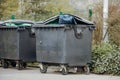 black trash container for waste, overload with garbage bags and open top cover, stand in urban city Royalty Free Stock Photo