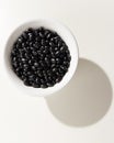 Black Turtle Bean legume. Grains in a bowl. Shadow over white ta