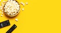 Black TV, audio remote control and popcorn on bright yellow background flat lay top view copy space. Minimalistic background with