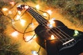 black ukulele guitar and christmas decorations on the dark background. hawaiian guitar with lighted garland on dark background.