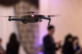 Black unmanned quadrocopter took off in a banquet hall with people on a blurred background. Royalty Free Stock Photo