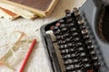 Black vintage metal type writer next to a pile of old note books, pair of eyeglasses and a pencil on a linen tablecloth