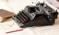 Black vintage metal type writer next to a pile of old note books, pair of eyeglasses and a pencil on a linen tablecloth Royalty Free Stock Photo