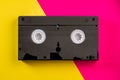 Black vintage VHS videotape cassette on yellow and pink background. Plastic retro video cassette with analog magnetic