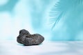 Black volcanic stone on turquoise pastel color background with shadows. Minimal creative concept. Podium for cosmetics.