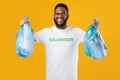 Black Volunteer Guy Holding Bags With Plastic Litter, Yellow Background