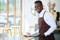 A black waiter or small restaurant operator invites customers to sit at the dining table