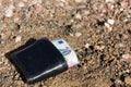 Black wallet on dirt ground with money