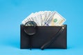 Black wallet with one hundred dollar bills and two hundred euro bil on a blue background. Checks dollar bills with a magnifying