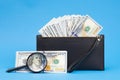 Black wallet with one hundred dollar bills and two hundred euro bil on a blue background. Checks dollar bills with a magnifying Royalty Free Stock Photo