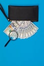 Black wallet with one hundred dollar bills and two hundred euro bil on a blue background. Checks dollar bills with a magnifying Royalty Free Stock Photo