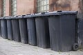 Black wheelie bins in a row on street with house numbers printed on front waiting for bin men to collect