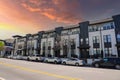 A black and white apartment building with trees in front and parked cars along the street with powerful red clouds at sunset Royalty Free Stock Photo